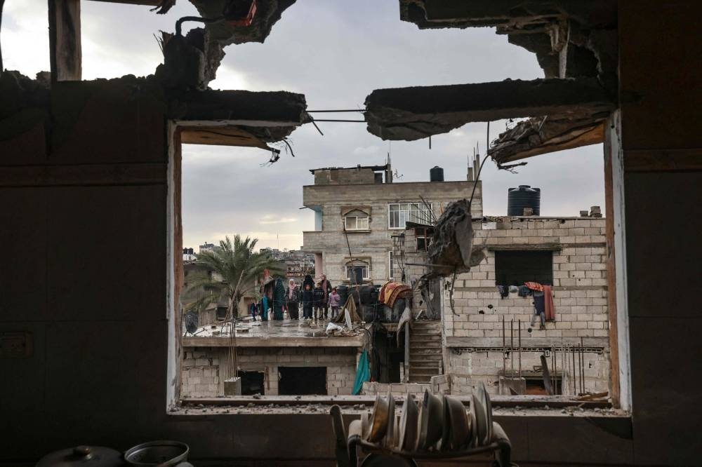 A picture taken through the window of a building damaged by Israeli bombing, shows members of a family standing on a rooftop, in Rafah in the southern Gaza Strip on Saturday. AFP