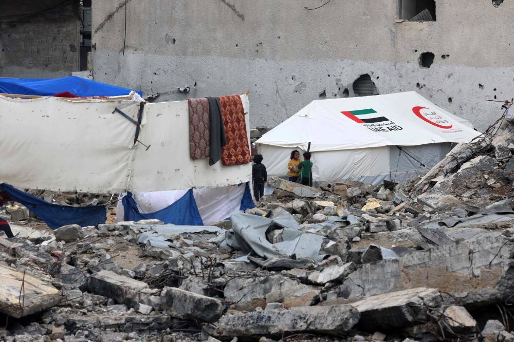 Palestinian children stand amidst rubble in front of a tent bearing the logo of the Emirati Red Crescent and the mention of the UAE aid, at a makeshift camp housing displaced Palestinians in Rafah in the southern Gaza Strip, on Sunday. AFP