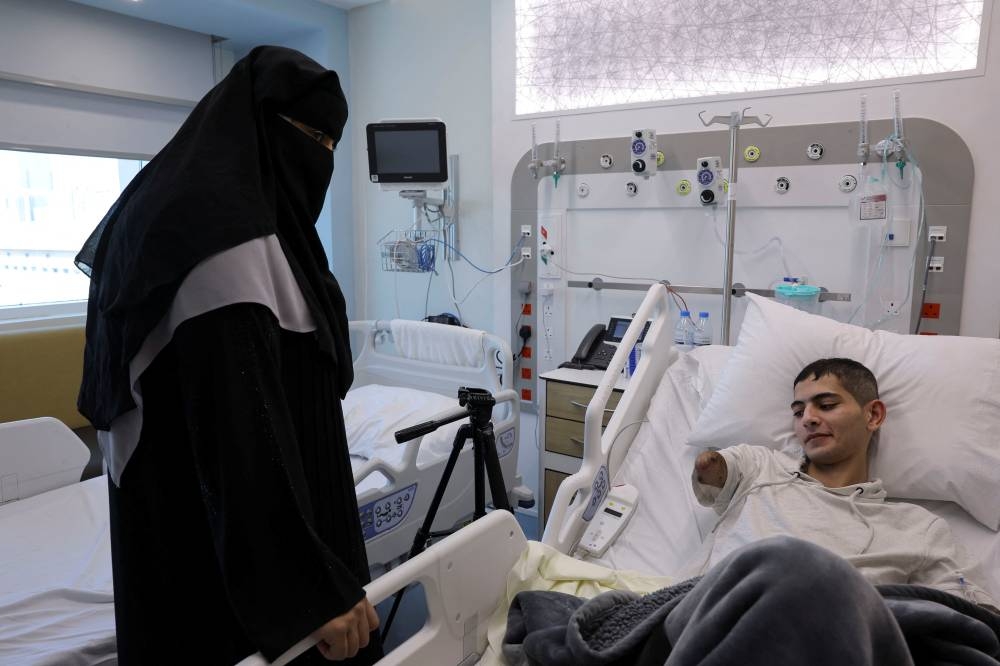 Palestinian Mohammad Al Jaafari, 18, who lost his arm to an Israeli airstrike and have multiple abdominal injuries, rests on a bed at a hospital, next to his mother, after both were evacuated from the strip by United Arab Emirates to receive medical care, in Abu Dhabi, on Tuesday. REUTERS