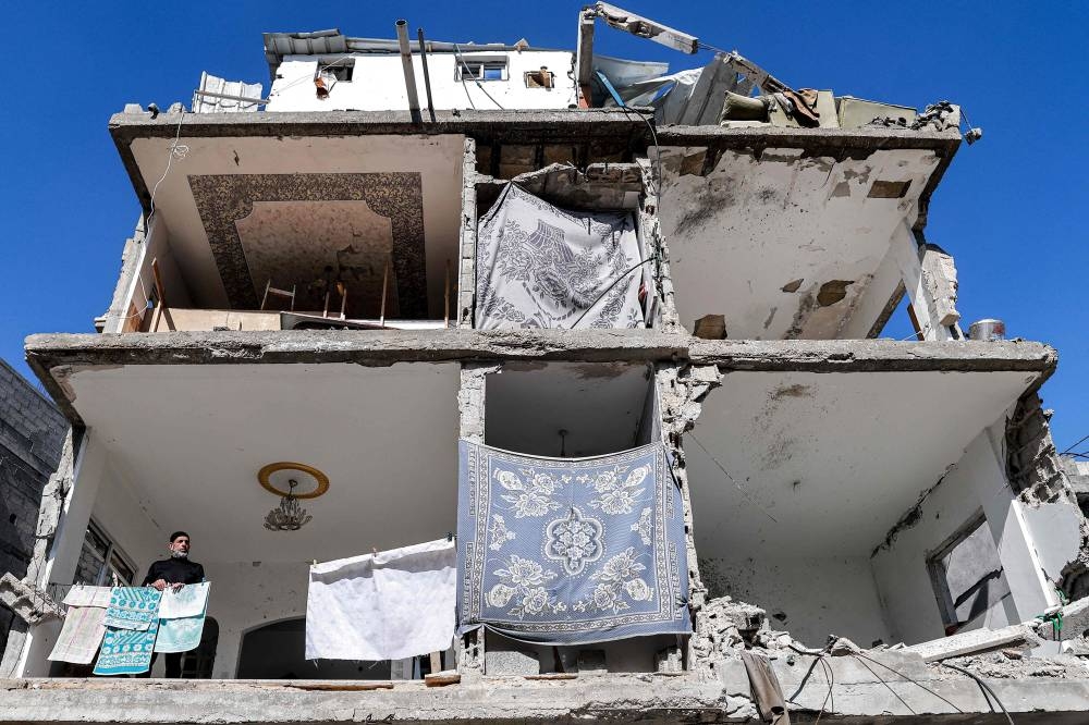 A man stands by towels hanging out to dry in a building with a destroyed facade that was damaged by Israeli bombardment, and in which bathrooms of individual flats are covered by blankets for privacy, in Rafah in the southern Gaza Strip on Tuesday. AFP