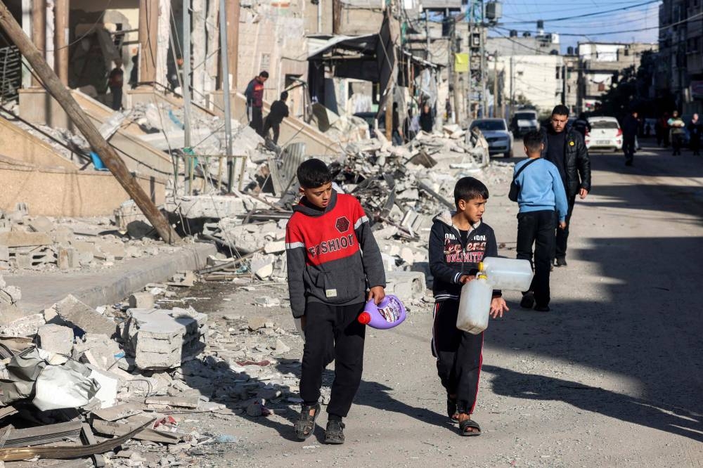 Children walk with plastic fluid containers past the rubble of a building that was destroyed during Israeli bombardment in Rafah in the southern Gaza Strip, on Wednesday. AFP