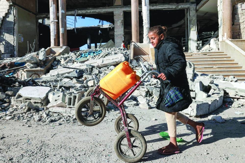 A girl pushes a cart loaded with a jerrycan while walking past the rubble of a building that was destroyed during Israeli bombardment in Rafah in the southern Gaza Strip, yesterday.