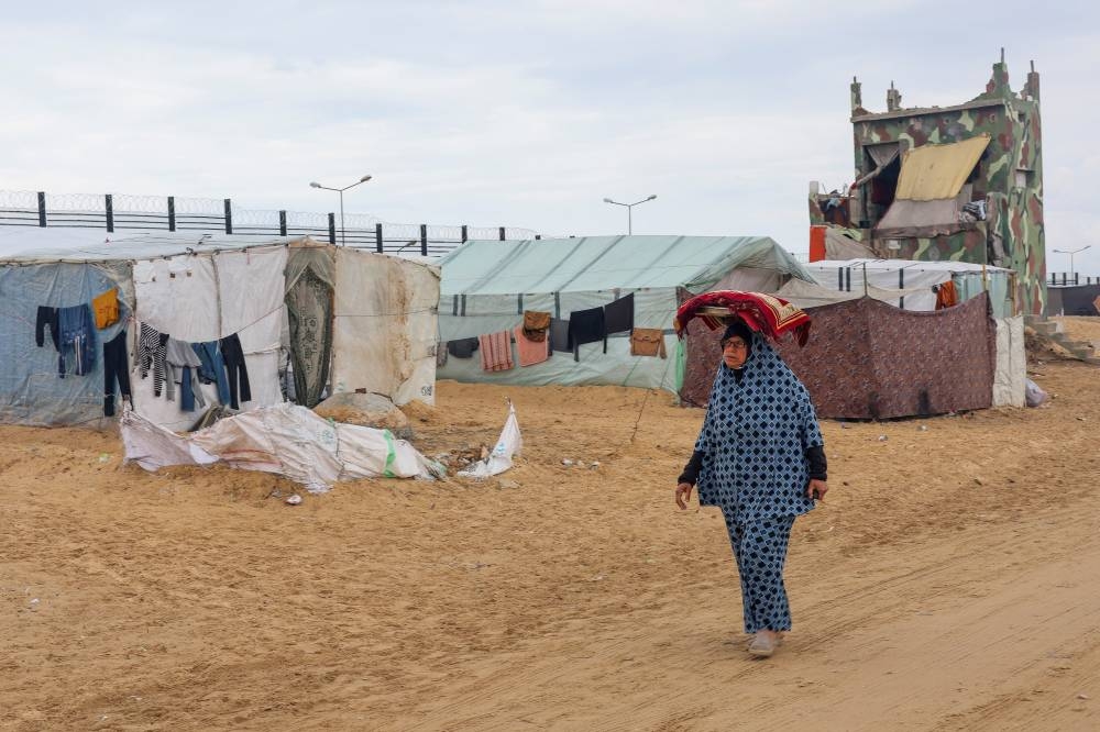 A displaced Palestinian woman, who fled her house due to Israeli strikes carries a tray with bread on her head as she walks past the border with Egypt in the southern Gaza Strip, on Sunday. REUTERS