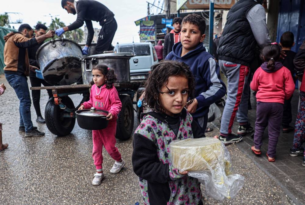 Displaced Palestinian children carry rations of red lentil soup, distributed by volunteers in Rafah in the southern Gaza Strip on Sunday. AFP