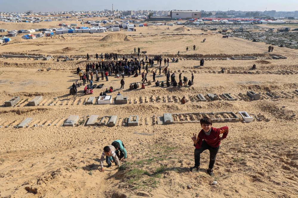 A Palestinian child gestures as people bury their dead who were killed during overnight Israeli strikes, at a cemetery in Rafah, on the southern Gaza Strip on Wednesday. AFP