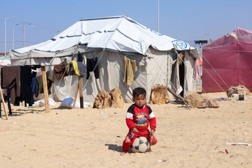 Displaced Palestinian boy, who fled his house due to Israeli strikes, sits on a ball, at a tent camp, near the border with Egypt, in Rafah in the southern Gaza Strip, Sunday. REUTERS