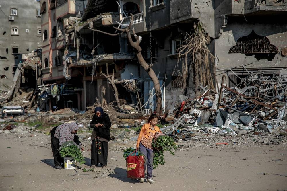 Palestinian women carry vegetables past buildings destroyed during Israeli strikes in Beit Lahia in northern Gaza, Monday.