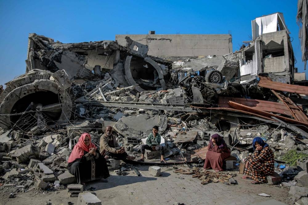 Palestinians sit next to a building destroyed during Israeli strikes in Gaza City, Monday.