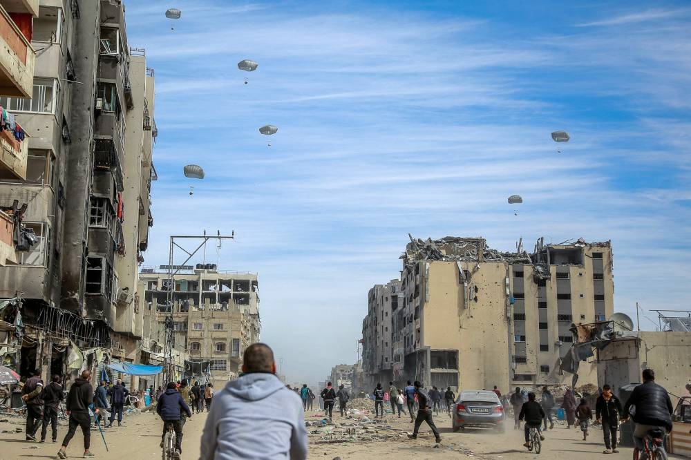 Palestinians run along a street as humanitarian aid is airdropped in Gaza City on Friday. AFP