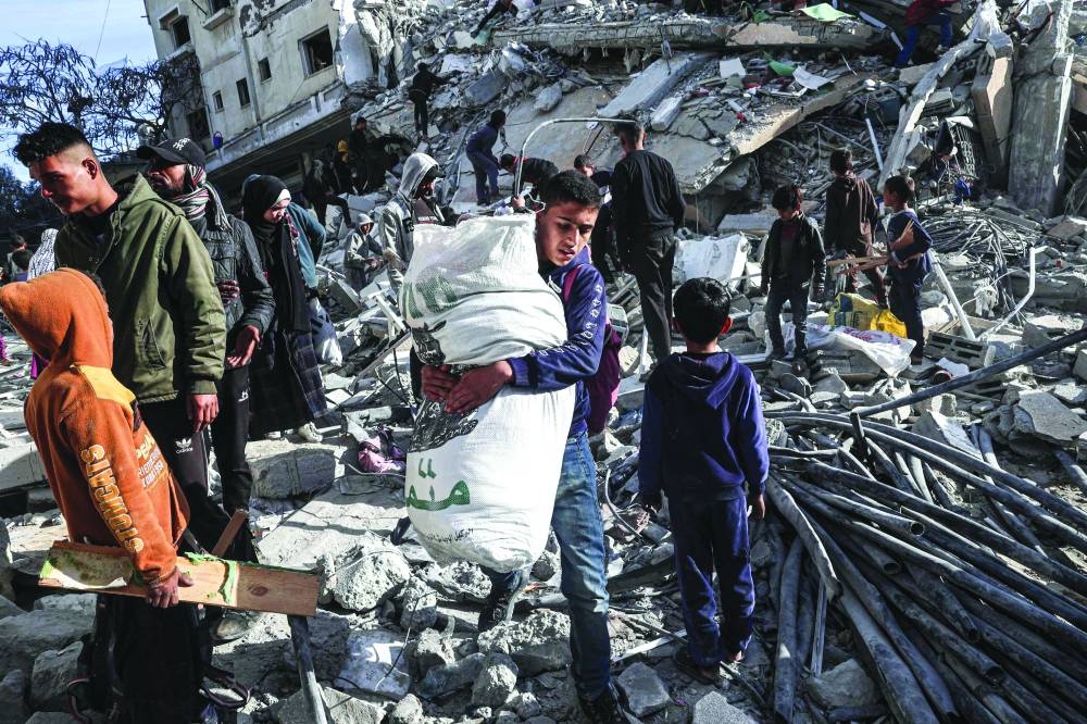 
A Palestinian youth walks away with some items salvaged from the rubble of a residential building hit in an overnight Israeli air strike in Rafah in the southern Gaza Strip, yesterday. 