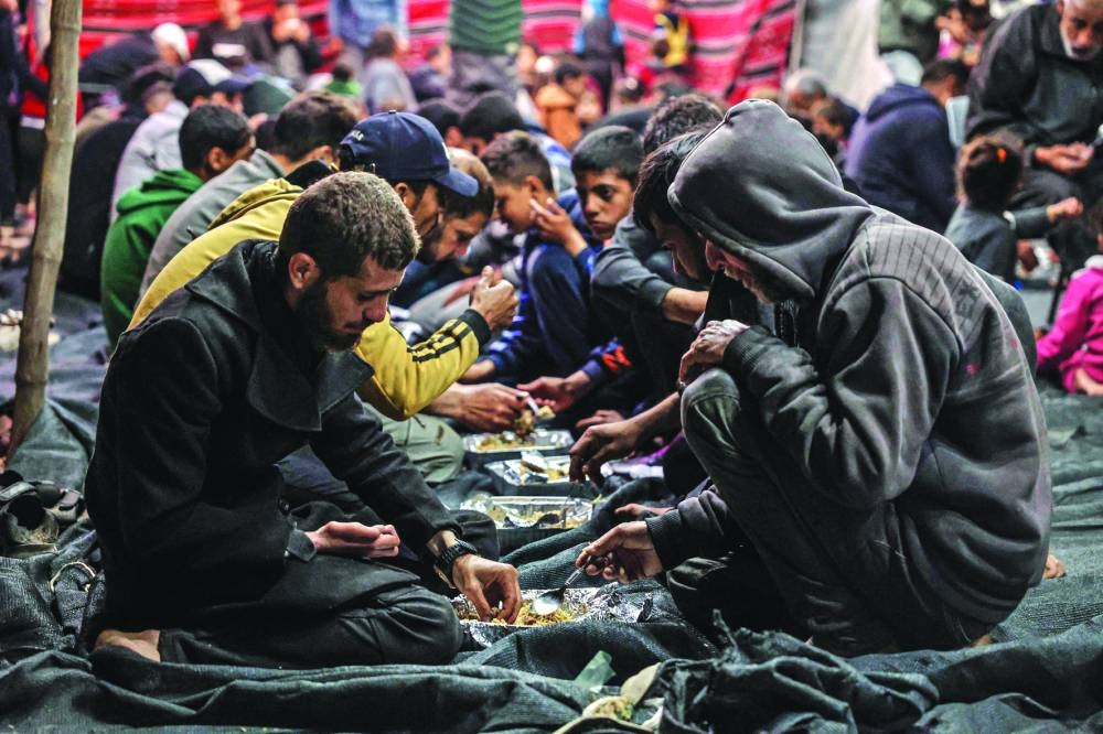 Palestinians share an Iftar meal, on the first day of the Muslim holy fasting month of Ramadan, at a camp in Rafah, on Monday. 