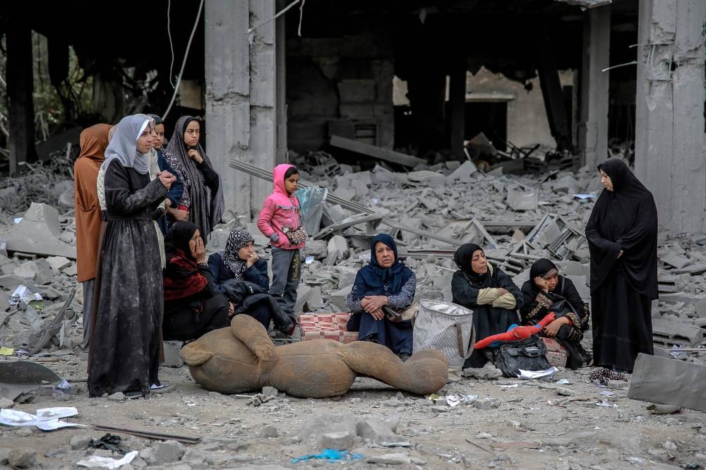 Palestinians sit next to the rubble of a building, after it was destroyed in an Israeli strike the night before, in the Rimal neighbourhood of Gaza City on Saturday. AFP