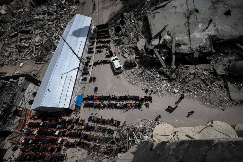 Palestinians perform the Friday noon prayers between the ruins of the Al-Faruq Mosque that was destroyed during Israeli bombardment and a structure built to temporarily replace the original building, in Rafah on the southern Gaza Strip on Friday. AFP