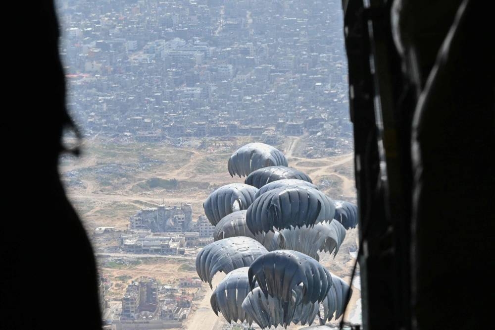 A picture taken Thursday onboard a US military transport aircraft shows humanitarian aid parcels attached to parachutes being airdropped over the Gaza Strip. AFP