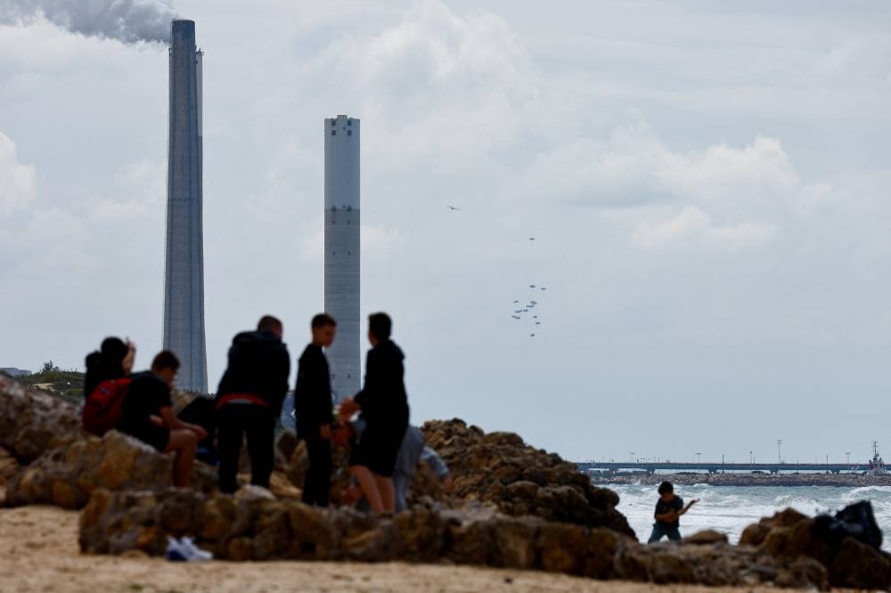 Children play at the beach as humanitarian aid falls through the sky towards the Gaza Strip in the background as seen from the city of Ashkelon, Israel, on Sunday. REUTERS