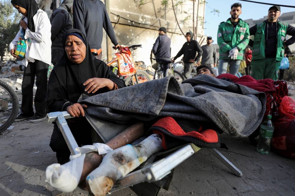 A woman reacts as she stands next to a wounded Palestinian lying on a bed at Al Shifa Hospital after Israeli forces withdrew from the hospital and the area around it. REUTERS