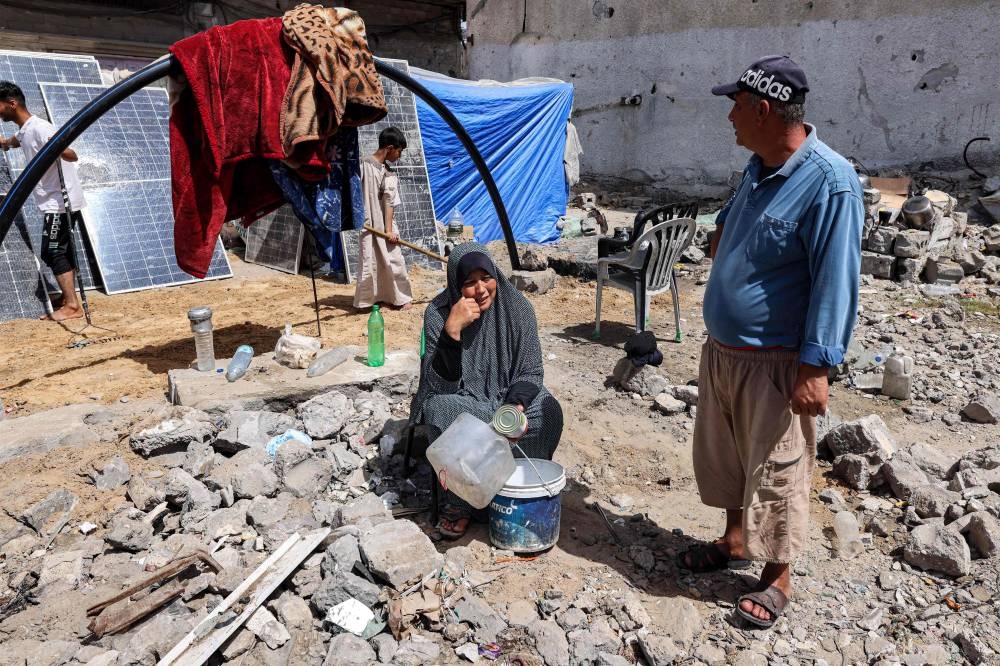 A woman sits holding empty containers outside a tent  in Rafah