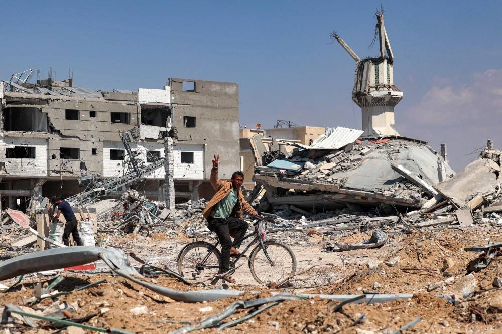 A man gestures as he rides a bicycle along a heavily damaged road past destroyed buildings in Khan Yunis on Sunday after Israel pulled its ground forces out of the southern Gaza Strip, six months into the devastating war. AFP