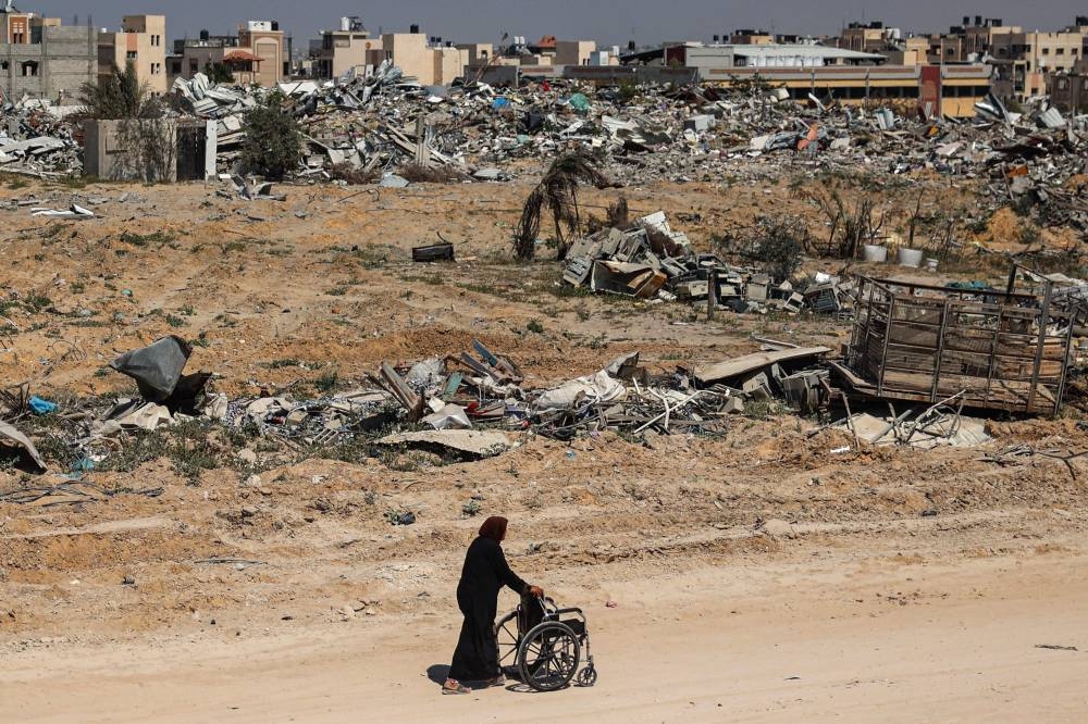 A Palestinian elderly woman pushes a wheelchair past rubble in Khan Yunis Sunday after Israel pulled troops out of the southern Gaza Strip.
