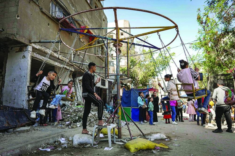  Children sit in a swing as they celebrate during the holiday of Eid al-Fitr, in Deir el-Balah in the central Gaza Strip.