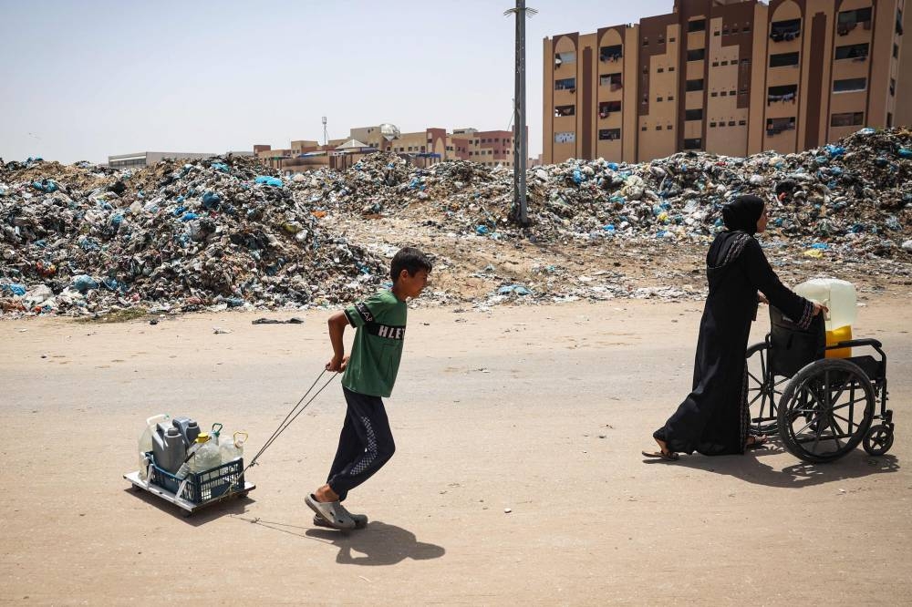 A child and a woman transport gallons of water as they walk past garbage piled up near tents set up by displaced Palestinians in Khan Yunis in the southern Gaza Strip, on Saturday. AFP