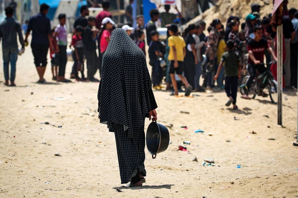 A displaced Palestinian woman carries an empty pan as she walks toward a food distribution point in Khan Yunis in the southern Gaza Strip, on Saturday. AFP