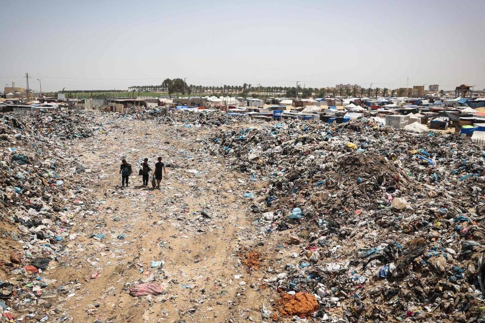 Children walk with bags of objects found in garbage piled up near tents set up by displaced Palestinians in Khan Yunis in the southern Gaza Strip, on Saturday. AFP