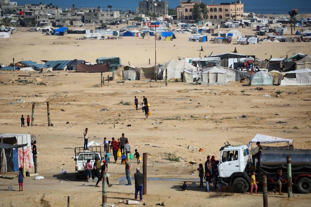 Displaced Palestinians carry water cans back to their tents at a temporary camp in Rafah on Friday. AFP