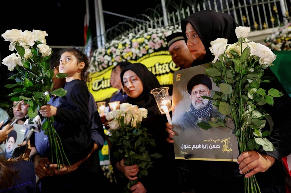 People holding flowers, candles, and pictures of the late Iranian President Ebrahim Raisi, attend a vigil to pay tribute to him and other victims who died in a helicopter crash,  outside the Iranian embassy in Jakarta, Indonesia. REUTERS