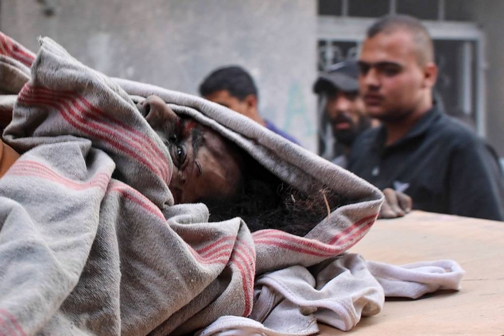 People stand next to the partially covered body of a Palestinian killed during Israeli bombardment at the Al-Daraj neighbourhood in Gaza City on Tuesday. AFP