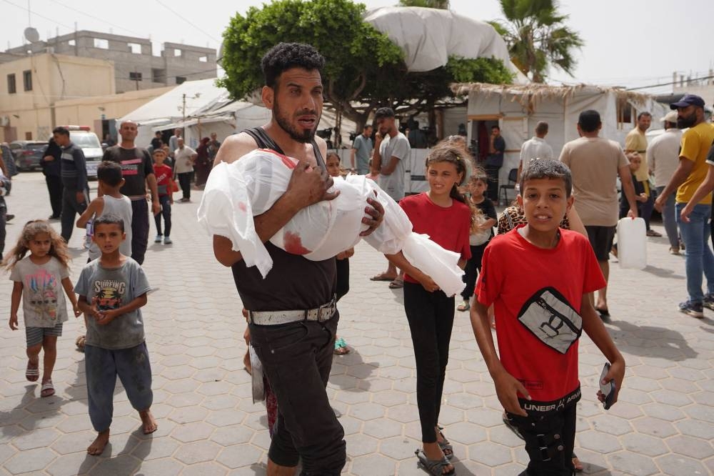 A Palestinian man carries the body of a child killed in Israeli bombardment on a house in Nuseirat city upon their arrival at the Al-Aqsa Martyrs Hospital in Deir al-Balah in the central Gaza Strip on Monday. AFP