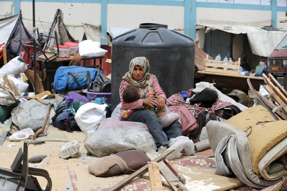 A woman sits with a child, on the day Palestinians travel on foot along with their belongings, as they flee Rafah due to an Israeli military operation, in Rafah, on Tuesday. REUTERS