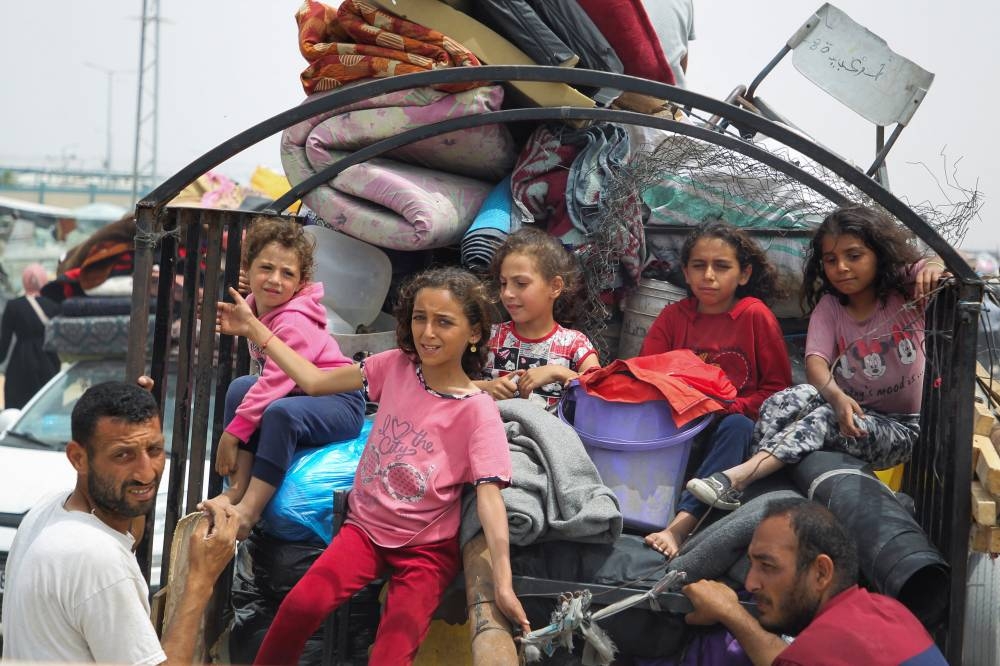 Children look on, as Palestinians travel on foot along with their belongings to flee Rafah due to an Israeli military operation, in Rafah, on Tuesday. REUTERS