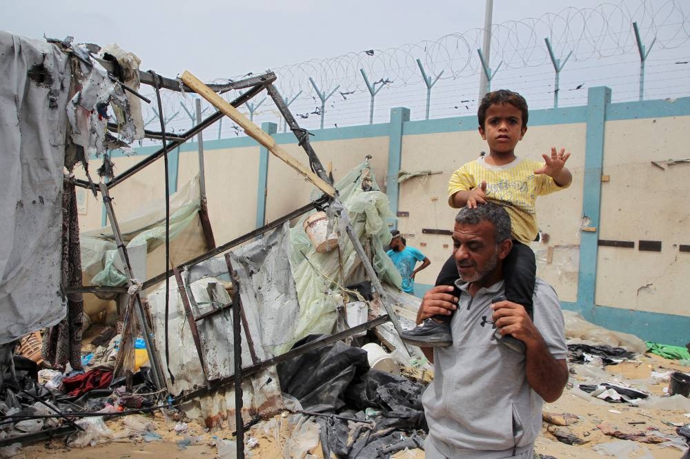 A child looks on as Palestinians inspect a tent camp damaged in an Israeli strike during an Israeli military operation, in Rafah, on Tuesday. REUTERS