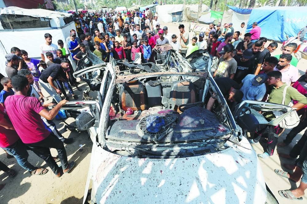 Palestinians inspect a vehicle hit in an Israeli strike, in Deir Al-Balah in the central Gaza Strip, Tuesday. 