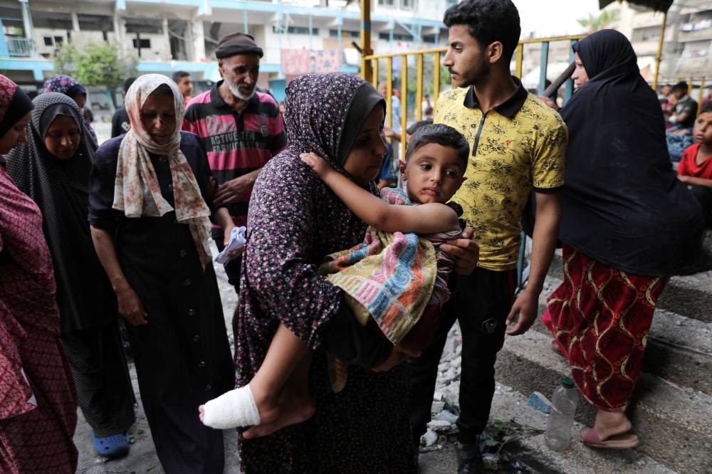 A woman carries a child at the site of an Israeli strike on a UNRWA school sheltering displaced people in Nuseirat refugee camp in the central Gaza Strip, Thursday. REUTERS