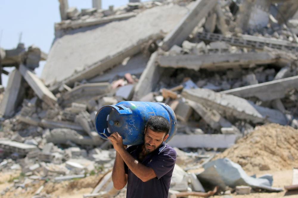A Palestinian man walks carrying a gas bottle on his shoulder past buildings destroyed in the Israeli bombardment of Khan Yunis, in the southern Gaza Strip on Tuesday. AFP