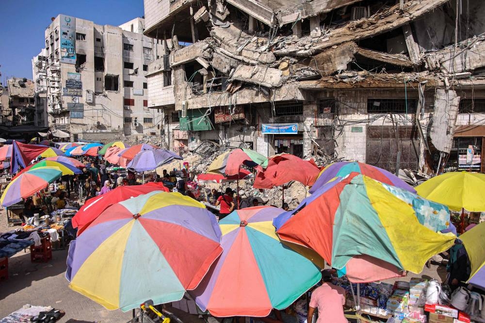 Vendors' umbrellas shade their stalls while erected before destroyed buildings along a market street in Gaza City on Sunday. AFP