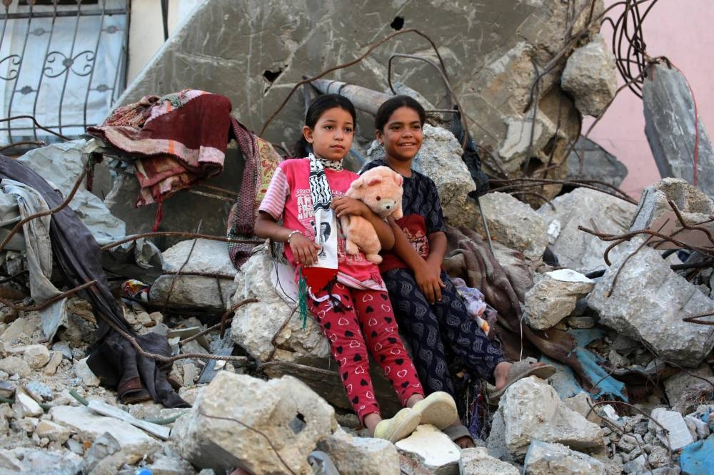 Palestinian girls, dressed in new clothes, lean against the rubble of a destroyed building as they celebrate the Eid al-Adha in Khan Yunis in the southern Gaza Strip, on Sunday. AFP
