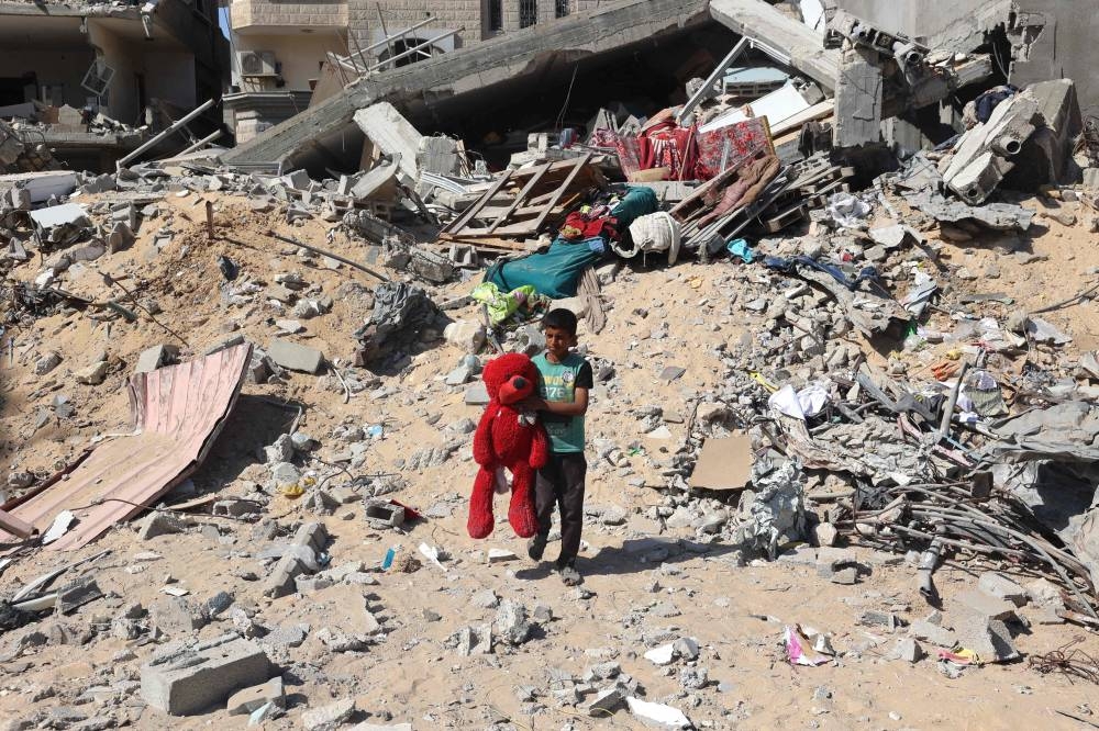 A Palestinian child walks with a stuffed bear recovered from the rubble of a destroyed building following Israeli bombardment in Khan Yunis, on Friday. AFP