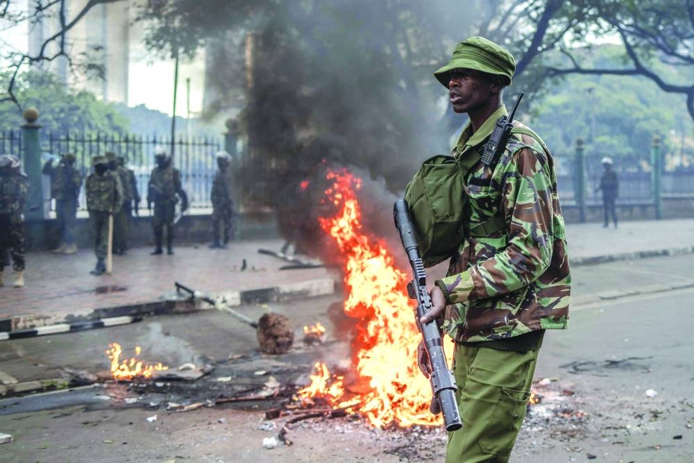 
A Kenyan Police Officer carrying a riot-control gun patrols next a barricade set alight by protesters. 