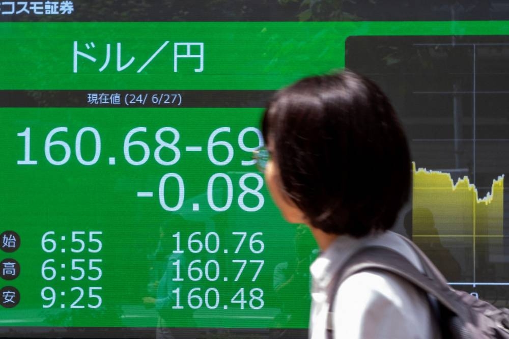 A woman walks past an electronic board displaying the exchange rate for the Japanese yen against the US dollar in Tokyo. The yen&#039;s latest retreat came as uncertainty surrounded the Federal Reserve&#039;s timetable for cutting interest rates, and the Bank of Japan&#039;s caution in tightening monetary policy.