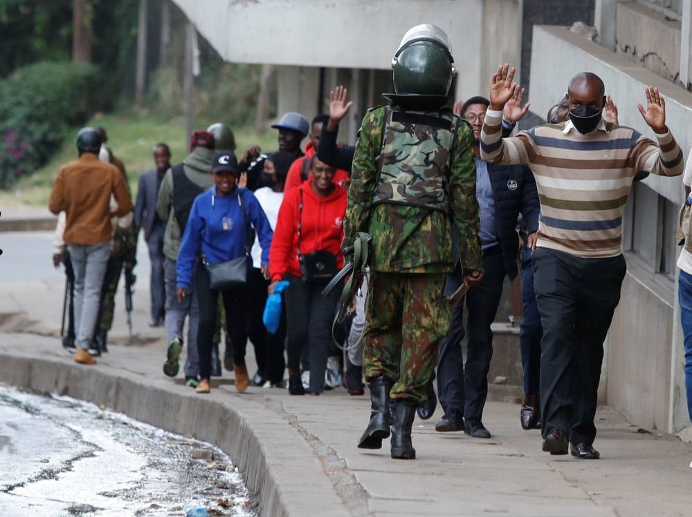 People lift their hands as they walk near a police officer during a demonstration over police killings of people protesting against Kenya's proposed finance bill 2024/2025, in Nairobi, Kenya, June 27, 2024. REUTERS/Monicah Mwangi