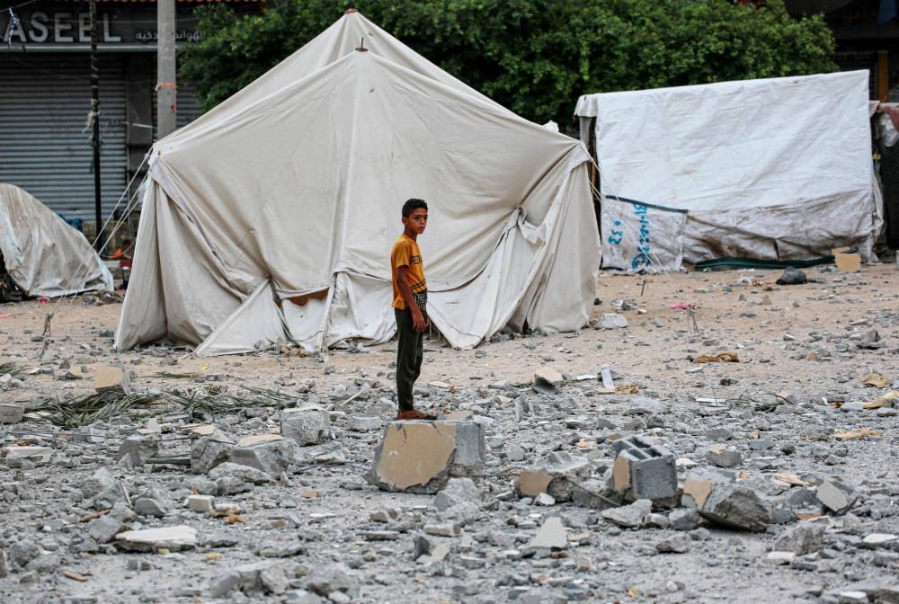 A Palestinian youth stands on rubble close to tents housing internally displaced people, erected in the square near the Deir al-Balah municipality building, destroyed following Israeli bombardment of Deir al-Balah, in the central Gaza Strip on Friday, AFP