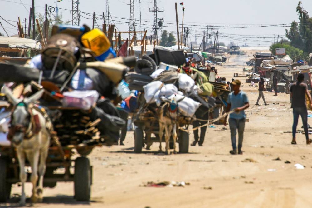 An Israeli tank takes position in the background as displaced Palestinians evacuate the Shakush area on the northwestern outskirts of Rafah, in the southern Gaza Strip, on Friday. AFP