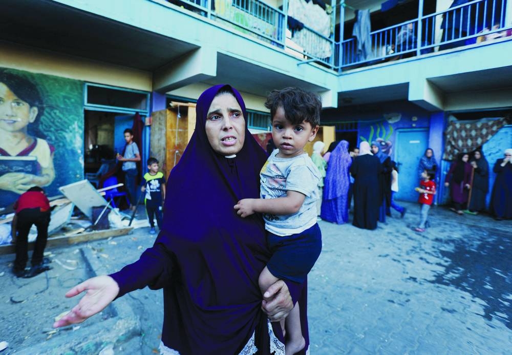 A Palestinian woman carrying a child reacts, after an Israeli air strike on a UN school in Nusairat in central Gaza Strip, Saturday.