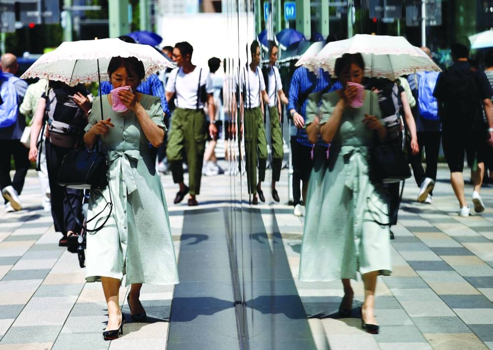 A passerby holding a parasol wipes her face as she walks on the street as the Japanese government issued a heatstroke alert in Tokyo and other prefectures, yesterday.