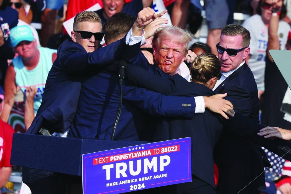 Former president Donald Trump gestures with a bloodied face while he is assisted by Secret Service personnel after he was shot in the right ear during a campaign rally at the Butler Farm Show in Butler, Pennsylvania. (Reuters)