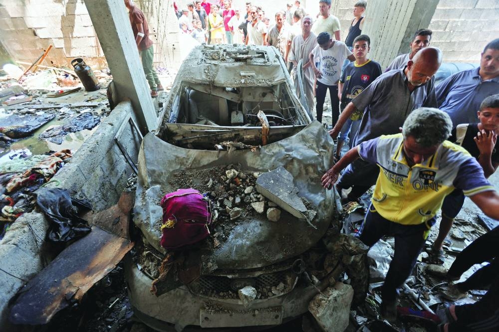 
People stand next to a damaged vehicle in a house hit in an Israeli strike, in Deir Al-Balah in the central Gaza Strip, yesterday. 