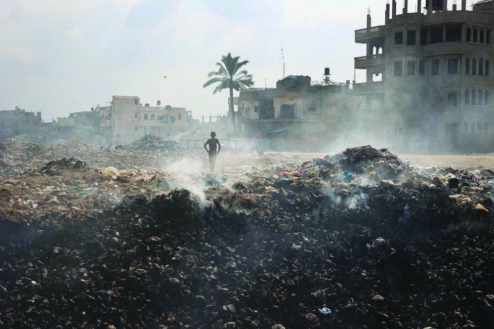 A Palestinian youth stand in the centre of piles of smouldering waste, as garbage collection and many other municipality services come to a halt due to the Israeli bombardment of the Gaza Strip, at the Al-Maghazi Palestinian refugee camp, in the central Gaza Strip.